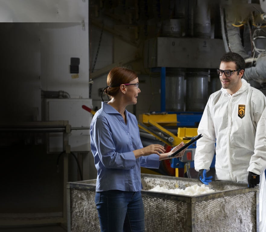 Worker wearing industrial protective coveralls and eyewear receiving instructions from female manager