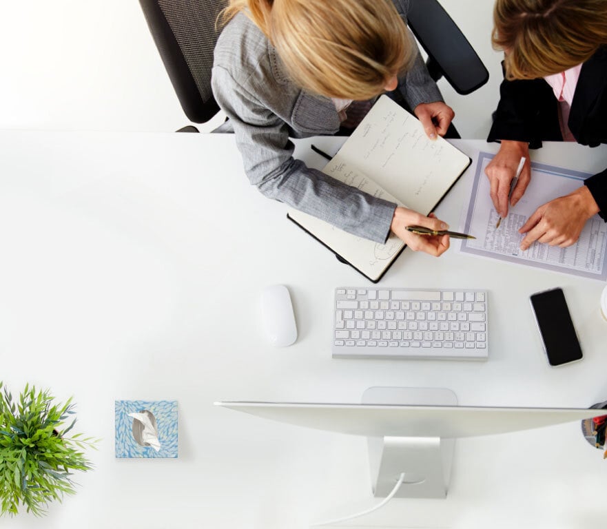 Overhead view of two professional women sitting at work desk discussing project