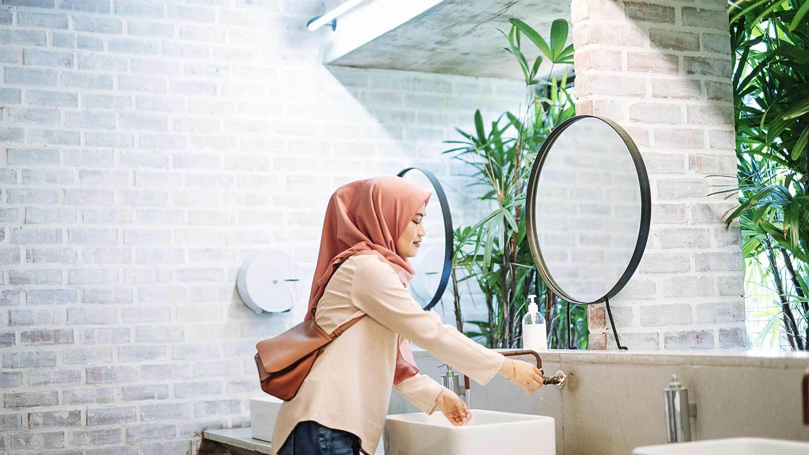Woman with headscarf using the sink in a restroom.