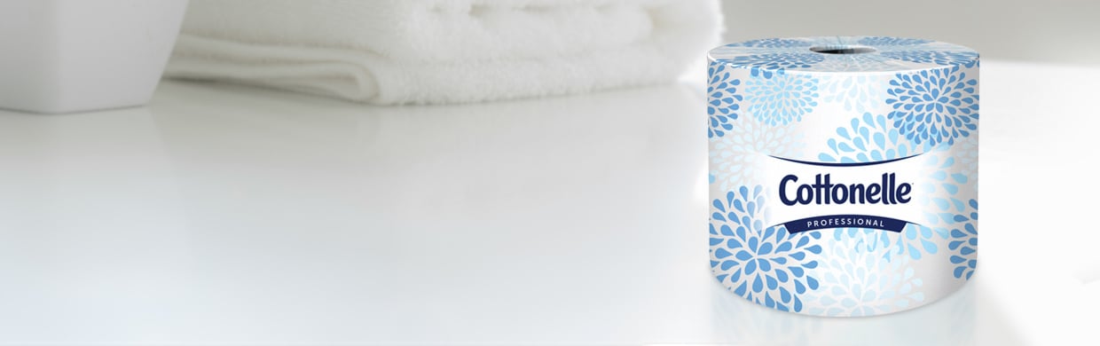 A roll of wrapped Cottonelle® toilet paper on a white countertop with a towel.