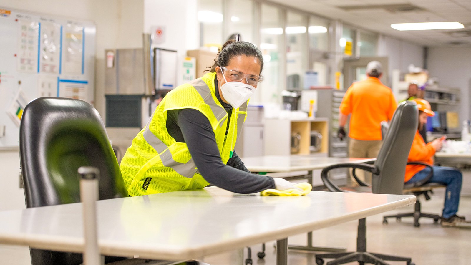 Female cleaner wearing mask wiping down table in break room