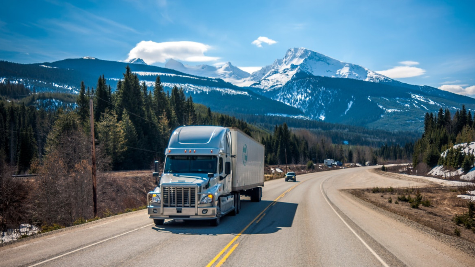 Freight truck traveling down open road with snow-peaked mountains in the background