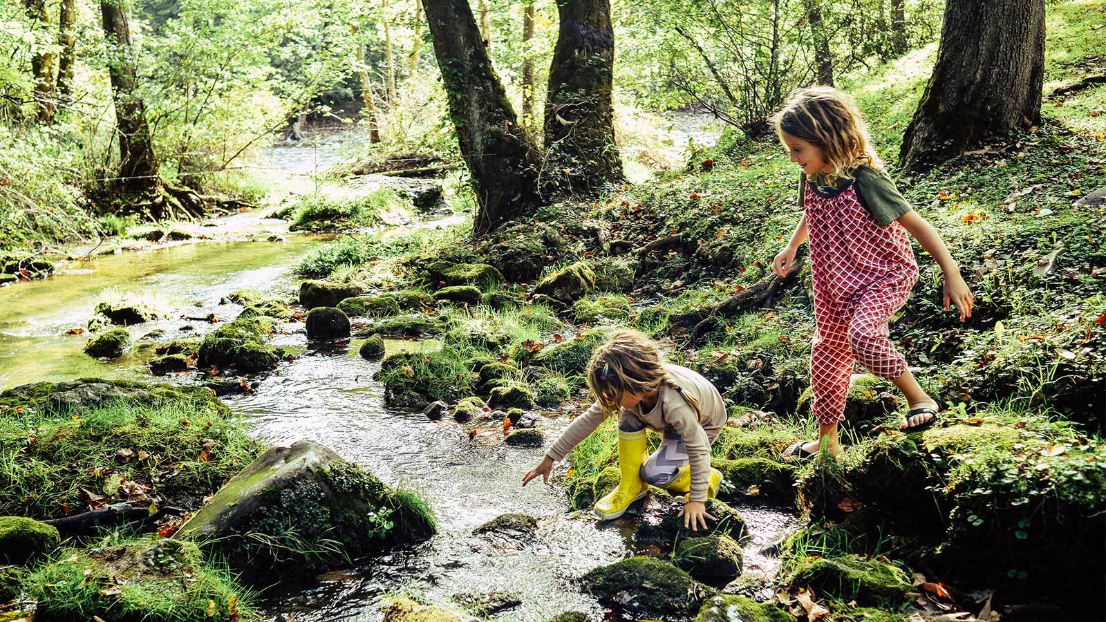 Little girl dipping hand in running stream as sister looks on.
