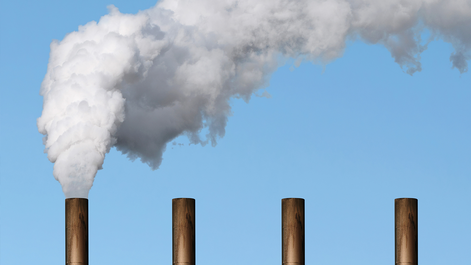 Four industrial smoke stacks with white smoke coming out of one