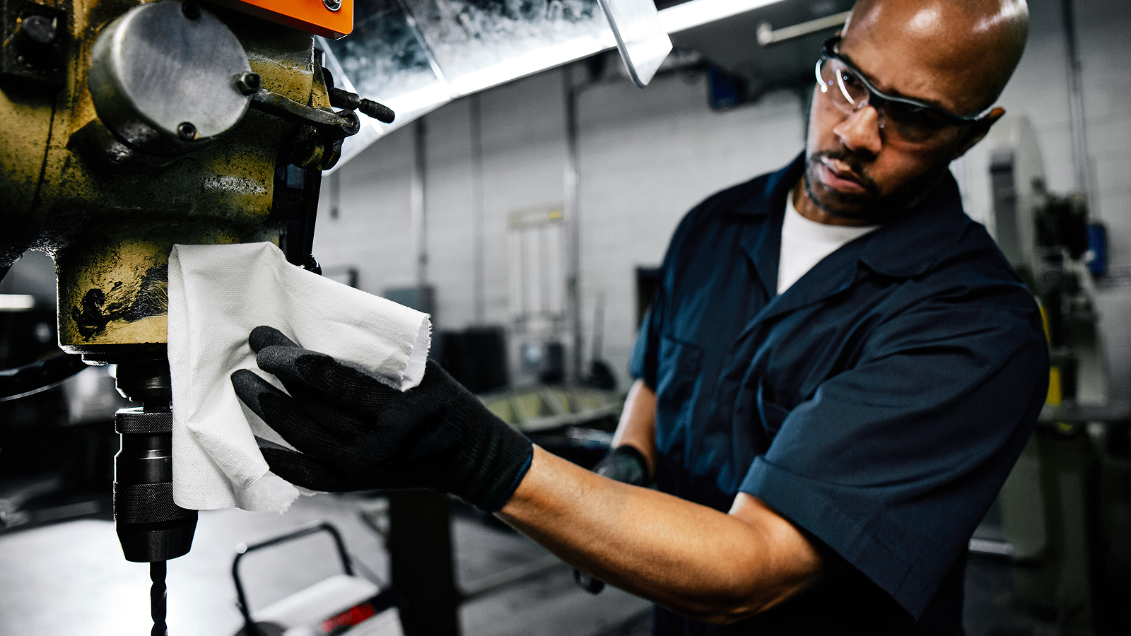 - Person wearing black gloves using a WypAll® cleaning cloth to wipe down industrial machinery.
